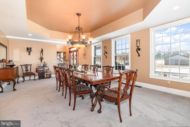 carpeted dining room with an inviting chandelier and a tray ceiling