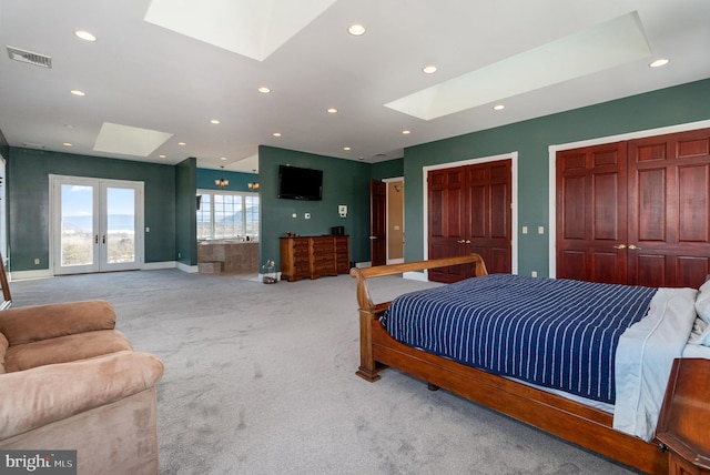 carpeted bedroom with french doors, two closets, access to exterior, and a skylight