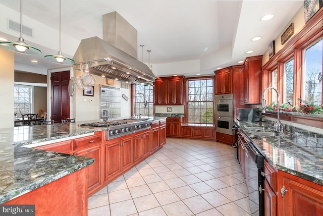 kitchen featuring sink, appliances with stainless steel finishes, dark stone countertops, hanging light fixtures, and island range hood