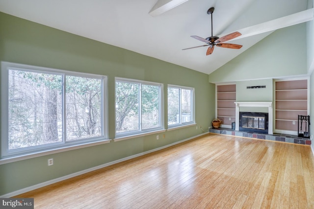 unfurnished living room with a tiled fireplace, vaulted ceiling with beams, a wealth of natural light, and built in features