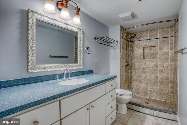 bathroom with a tile shower, vanity, tile patterned floors, and toilet