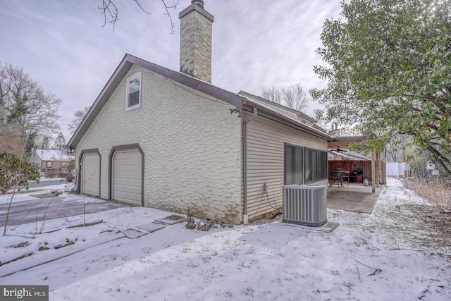 view of snow covered exterior featuring a garage and central AC