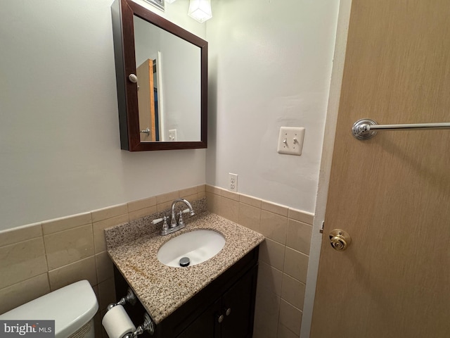 half bathroom featuring toilet, wainscoting, vanity, and tile walls