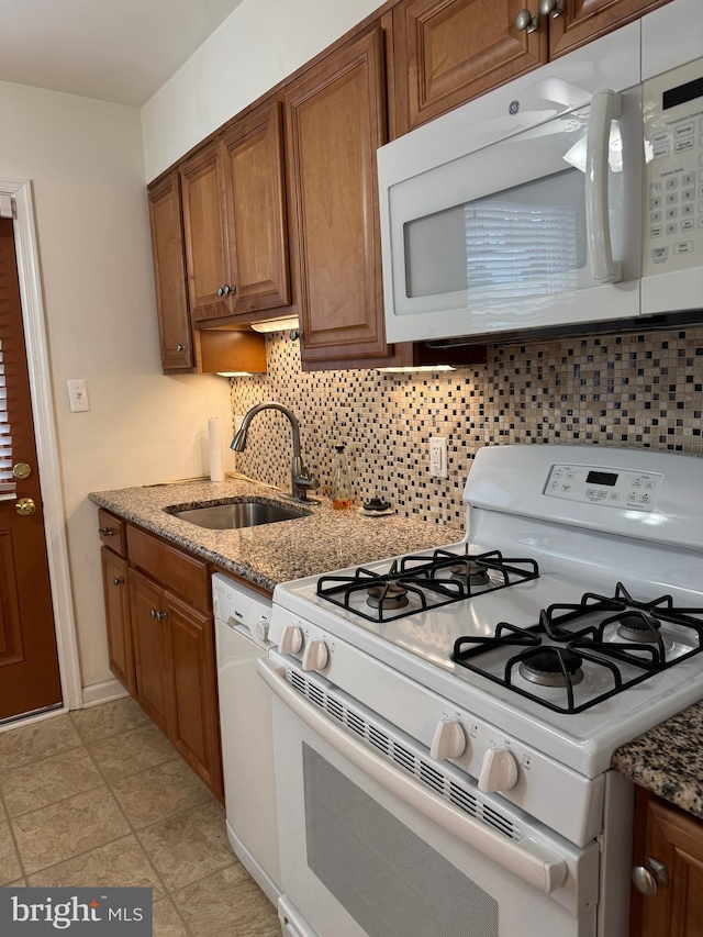 kitchen featuring white appliances, a sink, decorative backsplash, light stone countertops, and brown cabinetry