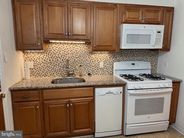 kitchen with white appliances, light stone counters, brown cabinets, and a sink