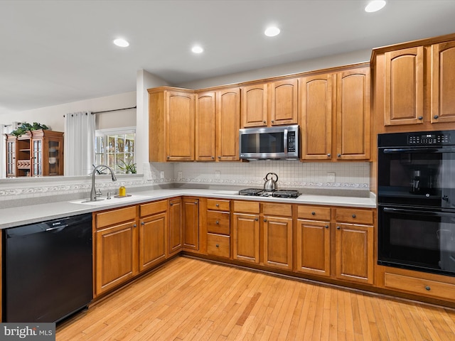 kitchen with light wood-type flooring, sink, decorative backsplash, and black appliances