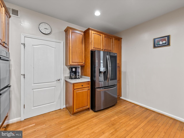 kitchen with double oven, light wood-type flooring, and stainless steel fridge with ice dispenser