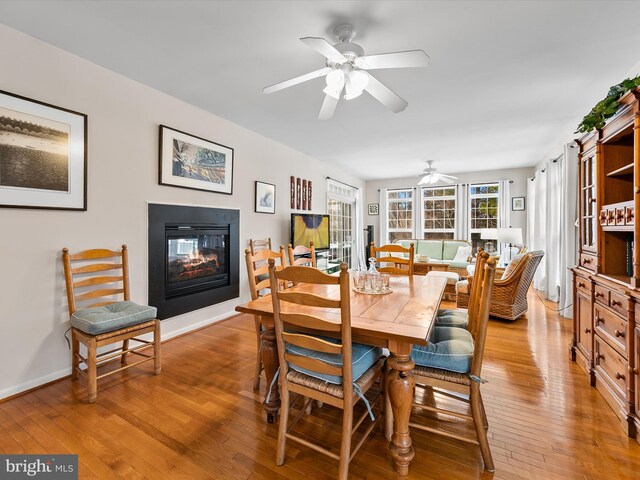 dining room featuring ceiling fan, a multi sided fireplace, and light hardwood / wood-style floors