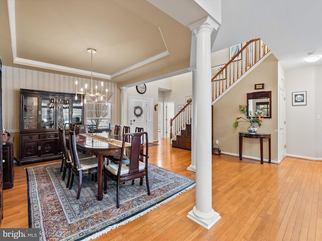 dining area with an inviting chandelier, wood-type flooring, a raised ceiling, and ornate columns