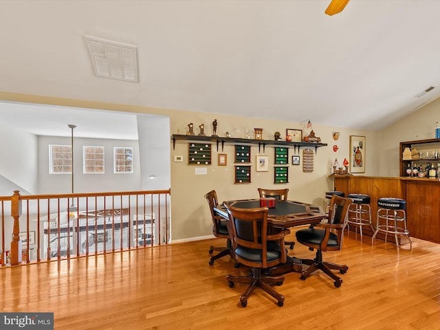 dining room with bar, wood-type flooring, and vaulted ceiling