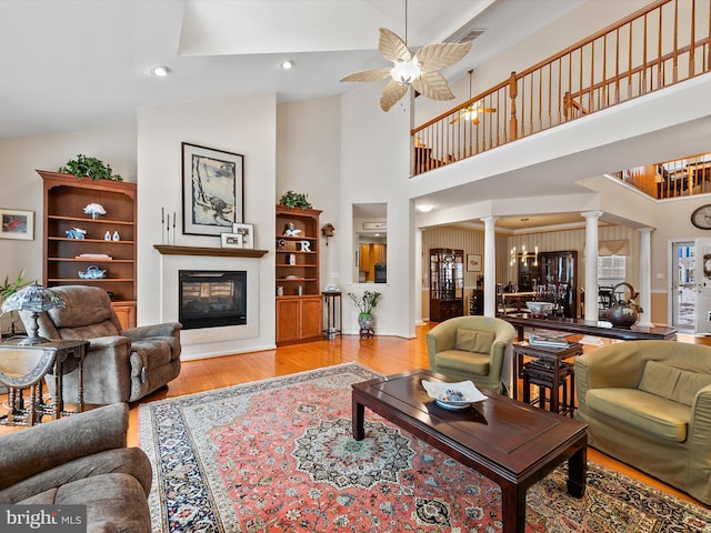 living room with ceiling fan, high vaulted ceiling, decorative columns, and light wood-type flooring