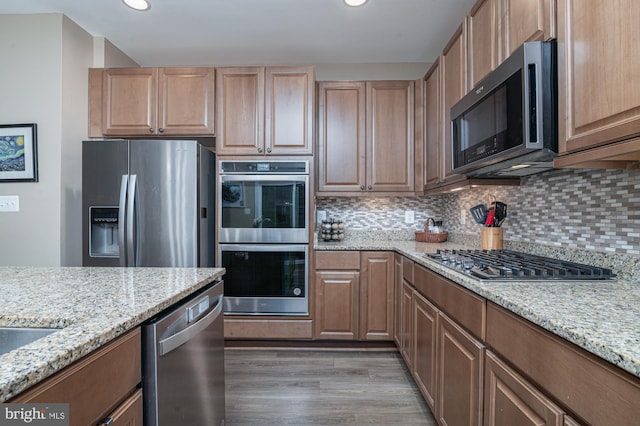 kitchen featuring tasteful backsplash, light wood-type flooring, light stone countertops, and appliances with stainless steel finishes