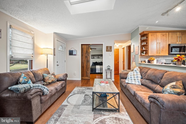 living room featuring ornamental molding, vaulted ceiling with skylight, light hardwood / wood-style floors, and a textured ceiling