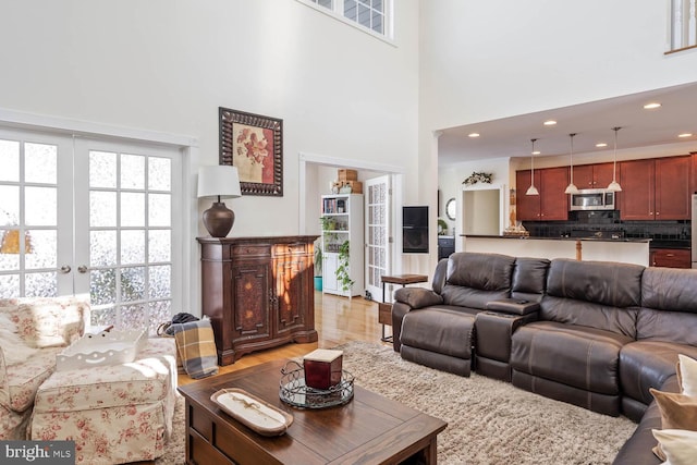 living room featuring a towering ceiling, light wood-type flooring, and french doors