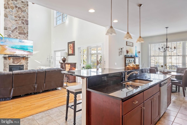 kitchen with a stone fireplace, a breakfast bar, pendant lighting, sink, and stainless steel dishwasher