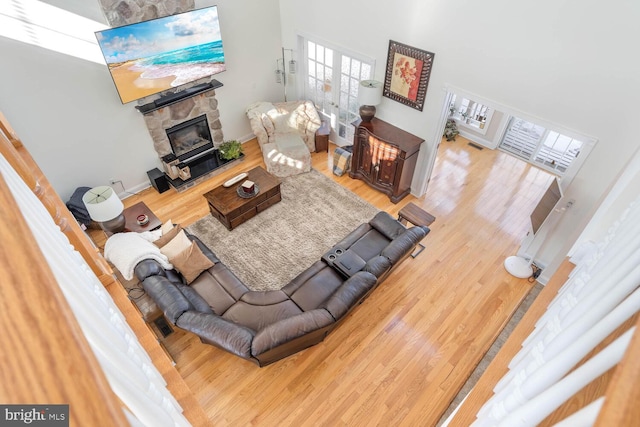 living room with a towering ceiling, wood-type flooring, and a stone fireplace