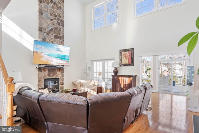 living room with light hardwood / wood-style flooring, a towering ceiling, a fireplace, and french doors