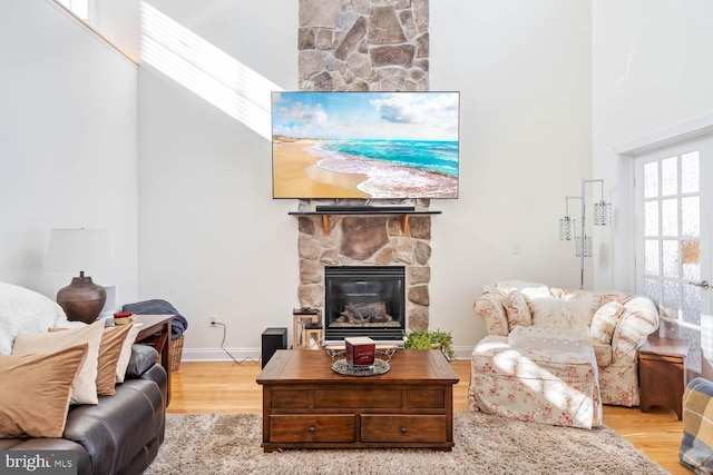 living room with a high ceiling, a stone fireplace, and hardwood / wood-style flooring