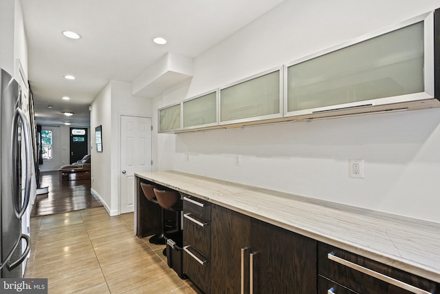 kitchen featuring light tile patterned floors, dark brown cabinets, and stainless steel refrigerator