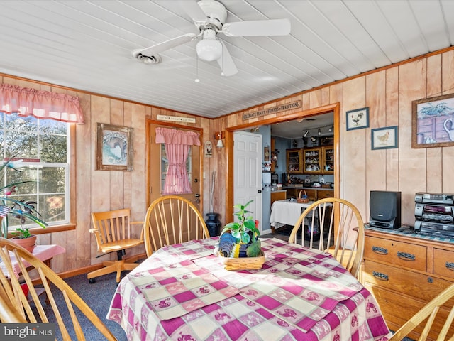 carpeted dining space with ceiling fan, wood ceiling, and wooden walls