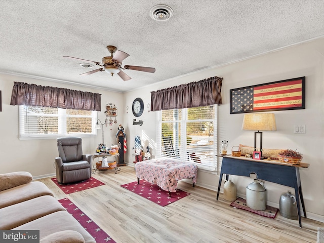 living room featuring a textured ceiling, ceiling fan, ornamental molding, and light hardwood / wood-style flooring