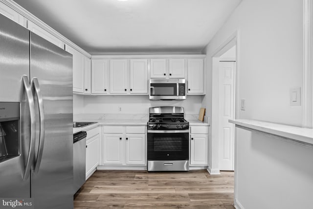 kitchen with light hardwood / wood-style floors, white cabinets, light stone counters, and appliances with stainless steel finishes