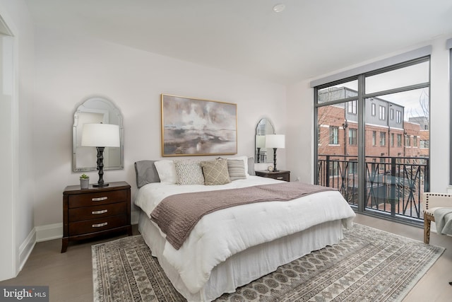 bedroom featuring a wall of windows, access to outside, baseboards, and wood finished floors