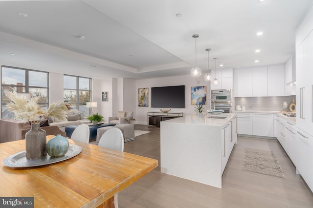 kitchen featuring white cabinetry, open floor plan, light countertops, backsplash, and an island with sink