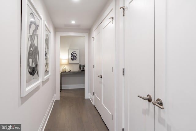 hallway with dark wood finished floors, visible vents, and baseboards