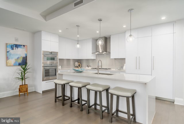 kitchen featuring wood finished floors, visible vents, a kitchen breakfast bar, light countertops, and wall chimney exhaust hood