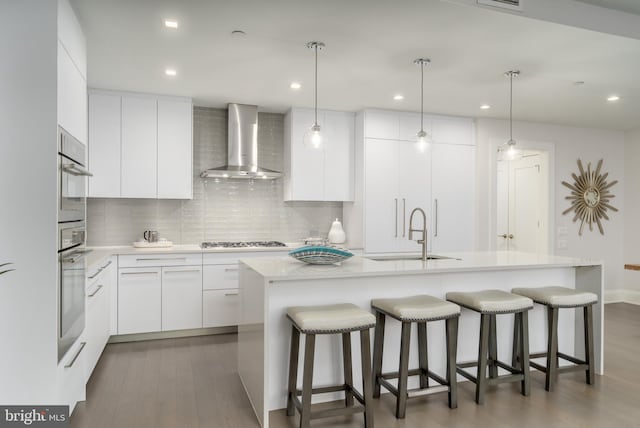 kitchen featuring light countertops, wall chimney range hood, a kitchen bar, gas cooktop, and a sink