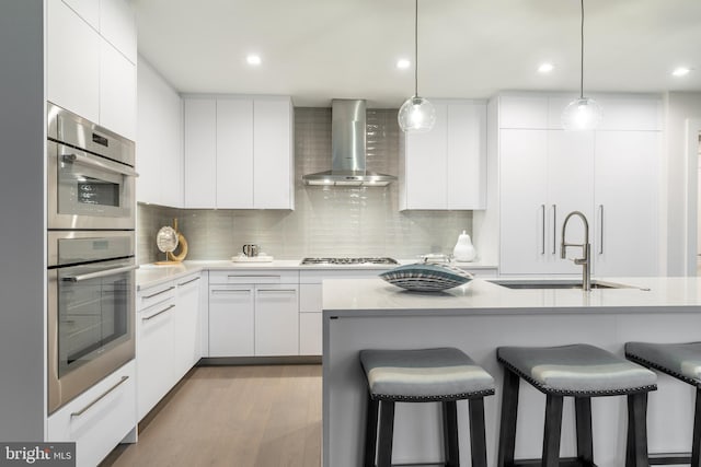 kitchen featuring wall chimney range hood, modern cabinets, a sink, and appliances with stainless steel finishes