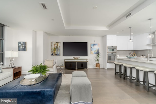 living room featuring baseboards, visible vents, a tray ceiling, and wood finished floors