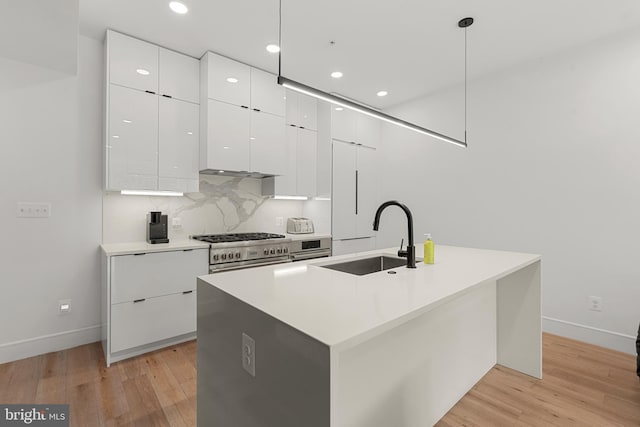 kitchen featuring decorative light fixtures, sink, white cabinets, and an island with sink