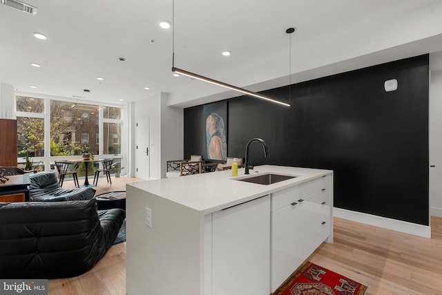 kitchen with pendant lighting, light hardwood / wood-style flooring, white cabinetry, sink, and a center island with sink