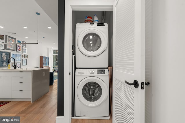 laundry area featuring sink, stacked washer and clothes dryer, and light hardwood / wood-style flooring