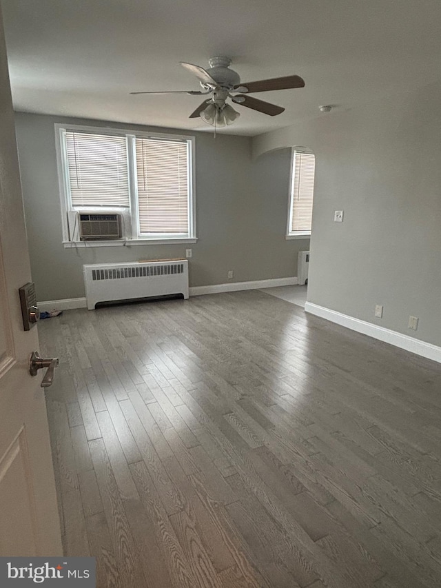 empty room featuring wood-type flooring, radiator heating unit, ceiling fan, and cooling unit