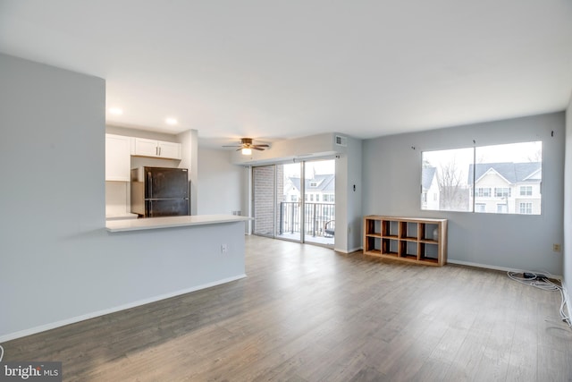 unfurnished living room featuring a ceiling fan, baseboards, and wood finished floors