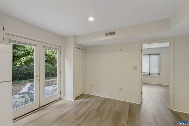 empty room featuring light wood-type flooring, a wealth of natural light, and french doors