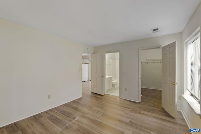 unfurnished bedroom with ensuite bath, light hardwood / wood-style flooring, a spacious closet, a closet, and white refrigerator