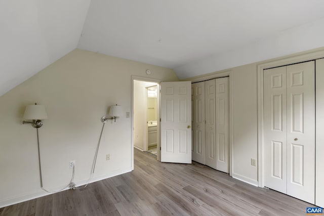 unfurnished bedroom with lofted ceiling, multiple closets, and light hardwood / wood-style floors