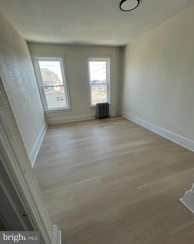 unfurnished room featuring radiator heating unit and light hardwood / wood-style floors