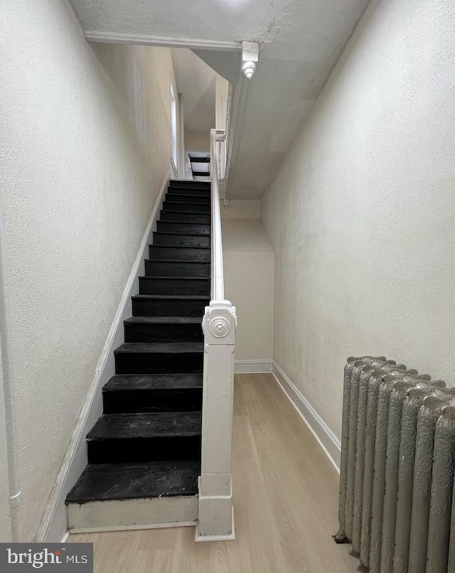 stairway featuring radiator and hardwood / wood-style flooring