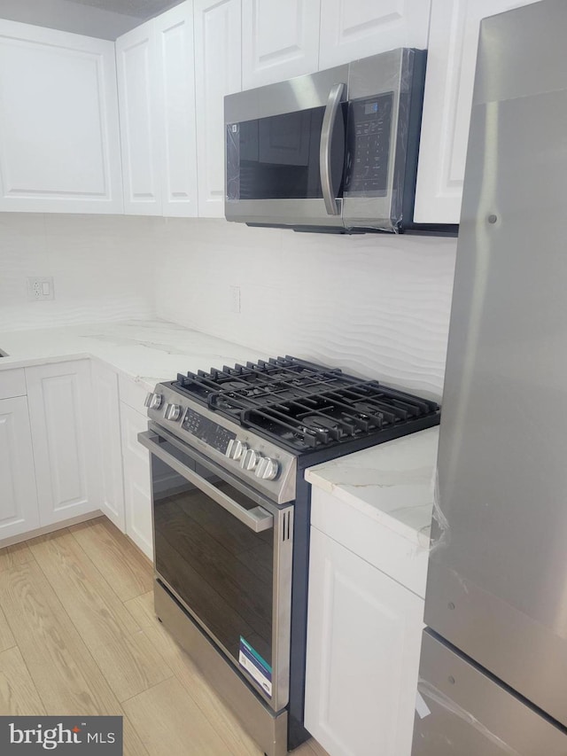 kitchen featuring white cabinetry, tasteful backsplash, light wood-type flooring, appliances with stainless steel finishes, and light stone countertops