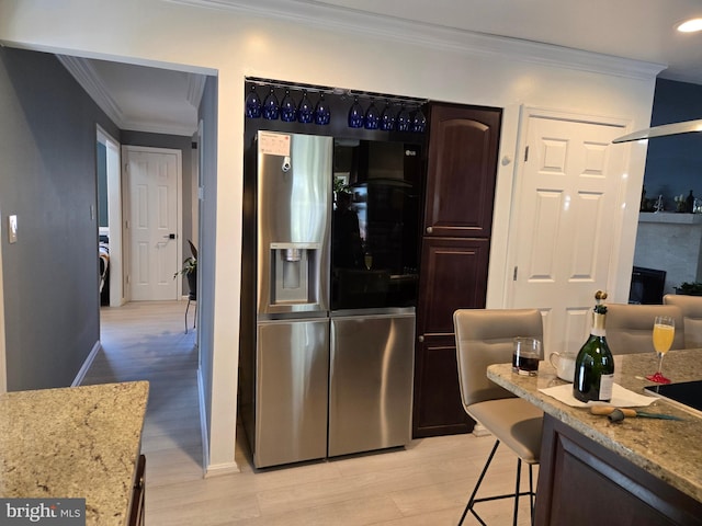 kitchen featuring stainless steel refrigerator with ice dispenser, dark brown cabinets, ornamental molding, light stone counters, and a breakfast bar area