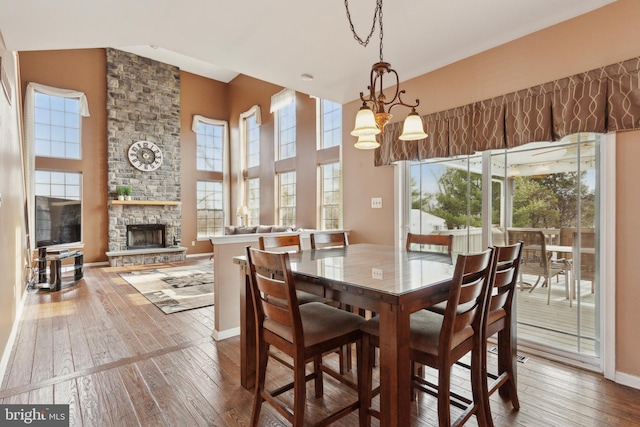 dining area featuring a high ceiling, baseboards, wood finished floors, and a stone fireplace