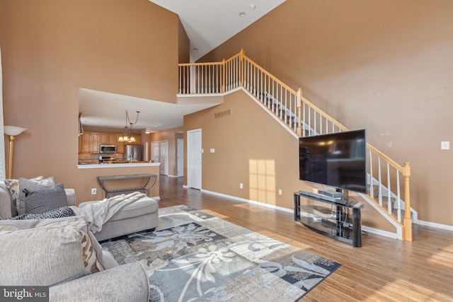 living room featuring baseboards, visible vents, a towering ceiling, stairs, and light wood-style floors