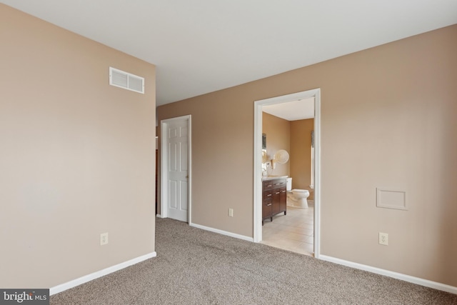 unfurnished bedroom featuring baseboards, ensuite bathroom, visible vents, and light colored carpet