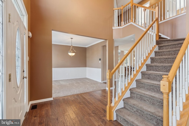 foyer entrance with a high ceiling, wood finished floors, visible vents, ornamental molding, and wainscoting