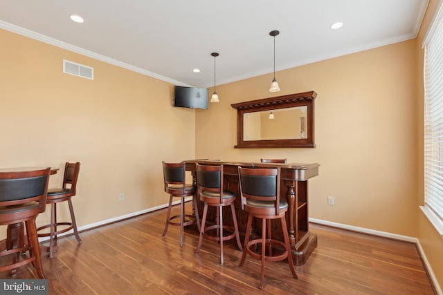 bar with visible vents, hanging light fixtures, dark wood-style floors, a bar, and crown molding